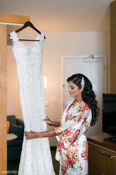 Lovely Indian bride looking at her white wedding dress. Lovely Indian bride looking at her white wedding dress.