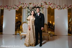 Indian couple posing at white and golden reception stage. Indian couple posing at white and golden reception stage.