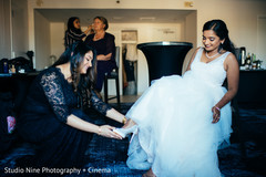 Indian bridesmaid helping bride getting her white shoes on. Indian bridesmaid helping bride getting her white shoes on.