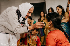 Senior Indian relative applying tumeric paste on Maharani's face Senior Indian relative applying tumeric paste on Maharani's face