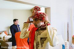 Indian groom in beige and red adjusting his turban Indian groom in beige and red adjusting his turban
