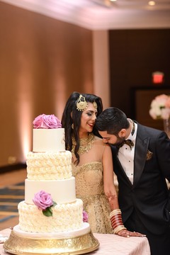 Indian couple posing next to white wedding cake. Indian couple posing next to white wedding cake.