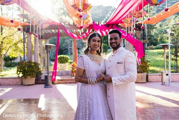 colorful wedding canopy,indian couple embrace,fuchsia orange drapes,vibrant wedding decor,soft romantic pose,cultural celebration,bright wedding setting,coordinated couple outfits,indian bride and groom,festive pre-wedding look