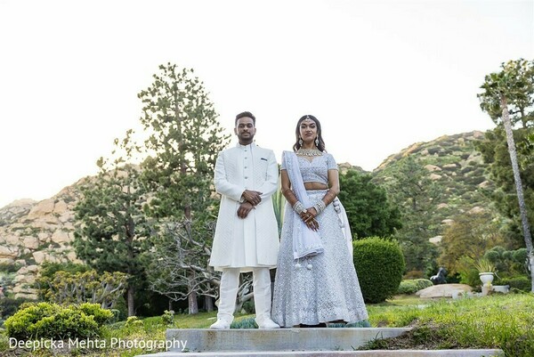 white indian wedding outfits,couple standing portrait,symmetrical bridal pose,serene landscape wedding,indian wedding elegance,stone pathway photo,wedding fashion minimalism,destination wedding frame,traditional white attire,natural light portrait