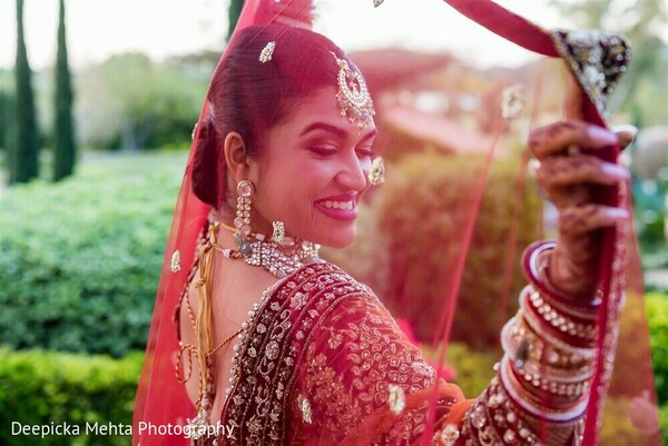 indian bride smiling,red bridal dupatta,over shoulder bridal pose,traditional indian jewelry,bridal lehenga joy,cultural bridal elegance,vibrant wedding portrait,veil lift photo,indian wedding style,glowing bride moment