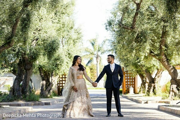 olive tree wedding,bride groom walking,indian bride and tuxedo groom,destination wedding couple,natural light walk,romantic wedding stroll,bridal lehenga moment,cinematic wedding scene,nature and tradition,elegant couple photo