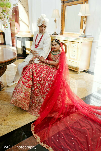bridal red veil drape,long lehenga train photo,bride sitting indoor pose,indian bridal elegance,red veil wedding shot,dramatic bridal styling,regal indian portrait,wedding editorial photo,cultural couture bridal moment,indoor bridal still