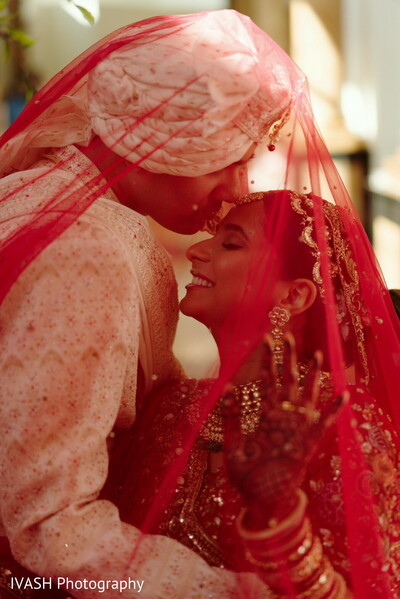 indian couple under veil,red silk bridal moment,intimate wedding portrait,forehead touch photo,romantic veil capture,hindu wedding emotional moment,bride groom closeness,cultural stillness photo,veil love frame,spiritual wedding touch