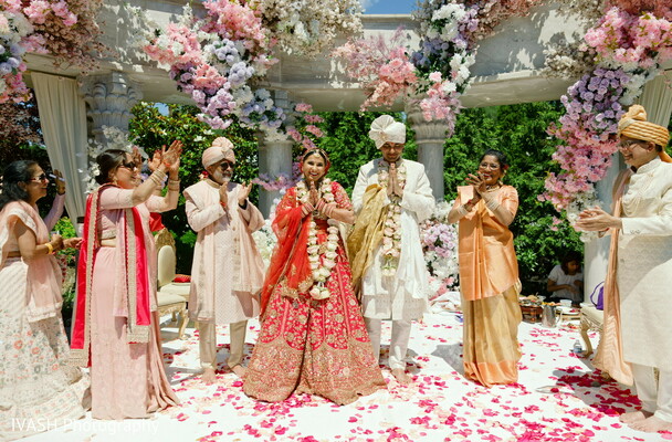 indian family wedding photo,group under mandap,floral altar family pose,hindu wedding group shot,cultural celebration portrait,red lehenga family ceremony,pink floral wedding scene,parents with bride groom,indian generational moment,sacred family unity
