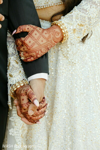 mehndi bride hands,wedding hand hold,indian wedding close-up,bride bangles detail,interlocked hands photo,groom holding bride,cultural wedding promise,bridal mehndi focus,love in touch photo,symbolic couple pose