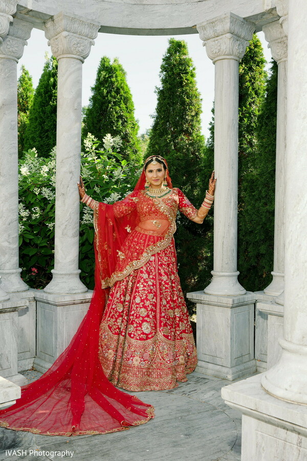 bride red lehenga marble,indian bridal pavilion,architectural bridal portrait,traditional indian elegance,wedding column backdrop,regal bridal styling,silk lehenga movement,cultural poise photo,wedding fashion composition,graceful indian bride