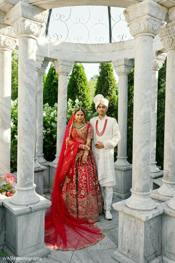 solo bride pavilion shot,red lehenga wedding pose,cultural column setting,indian wedding architecture,bridal elegance moment,fashion and tradition,marble and mehndi,bridal center frame,regal cultural bridal portrait,wedding landmark setting