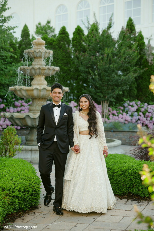 bride groom fountain,outdoor garden wedding,indian couple spring photo,nature wedding romance,floral greenery portrait,cultural love story image,garden venue moment,bridal gown outdoors,tux groom photo,peaceful wedding pose