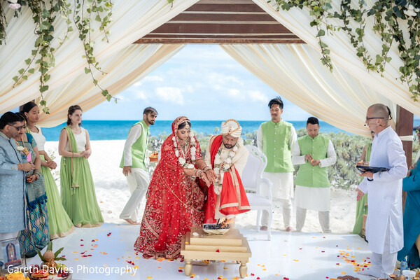 wedding mandap with guests,indian bridal party ceremony,beach vows group photo,family at wedding altar,tropical destination wedding,indian couple ocean canopy,floral wedding setup,bridesmaids and groomsmen indian wedding,love celebration circle,seaside mandap team