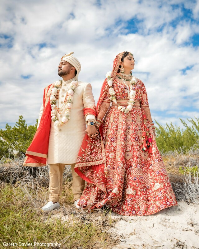 indian wedding beach photo,bride groom walking portrait,windswept wedding photo,red lehenga outdoor,destination wedding couple,elegant indian attire,nature meets tradition,indian wedding magazine-style shot