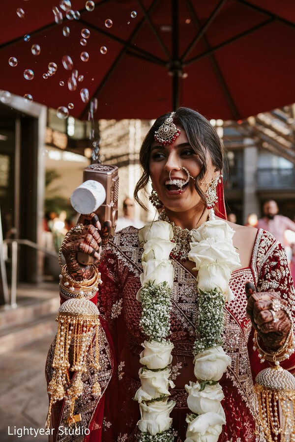 indian bride,wedding flowers,floral shower,vibrant umbrella,joyful bride,wedding traditions,candid bridal moment.