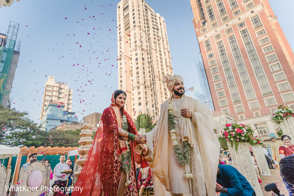 indian vidaai with confetti,urban indian wedding,bride groom city backdrop,cultural wedding exit,south asian farewell moment,modern wedding setting,confetti wedding photo,skyscraper wedding image,indian tradition in city,joyful wedding farewell
