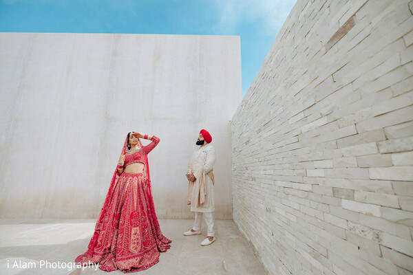 couple walking photo,indian wedding photoshoot,white wall background,bride groom stroll,wedding portraits,red bridal lehenga,minimalist wedding setting,sikh couple portrait,modern wedding aesthetic,holding hands photo