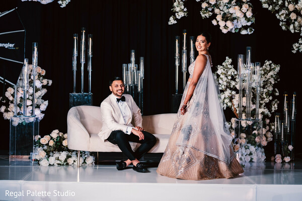 reception stage couple,floral wedding backdrop,indian reception photo,wedding couple on stage,white floral decor,glam reception look,bride groom celebration,modern indian wedding,luxury floral setup,spotlighted love