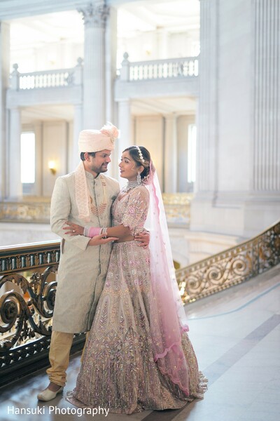 couple at marble balcony,romantic wedding pose,bride groom elegant photo,indian wedding venue,classic architecture couple shot,pastel wedding outfit,bride veil flying,wedding calm moment,balcony view shot,love and stillness