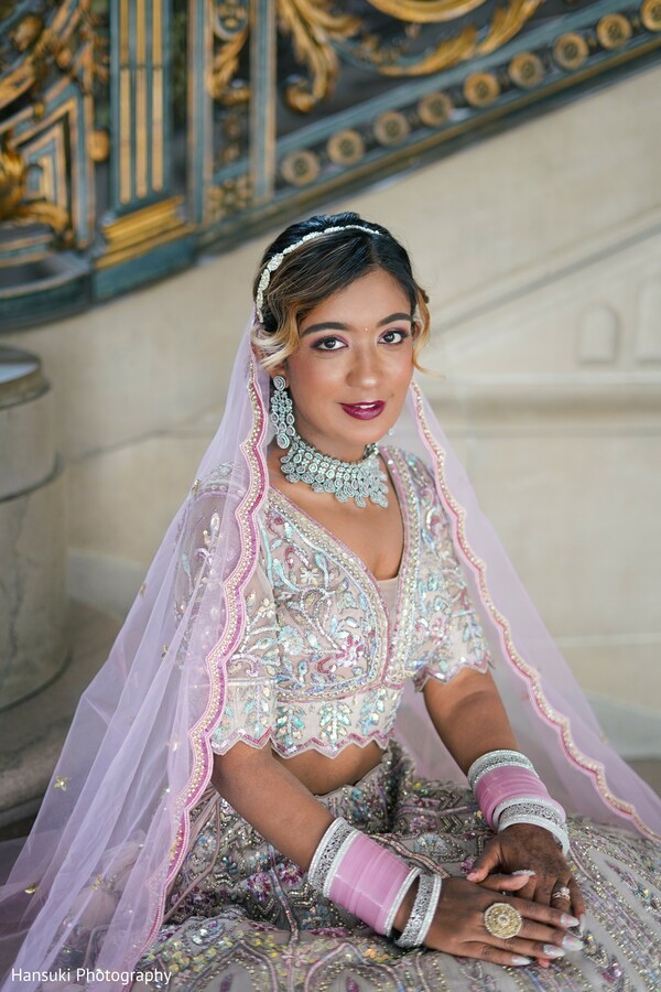 solo bridal portrait,pastel lehenga bride,ornate wedding bench,traditional indian bride,bridal jewelry and smile,soft wedding moment,seated bridal pose,elegant pink lehenga,south asian bride styling,classic indoor bridal phot