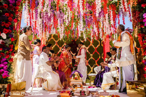 colorful indian mandap,south indian wedding ceremony,family and rituals,floral wedding stage,traditional wedding setup,hindu marriage customs,vibrant wedding celebration,ceremony in progress,wedding party together,full cultural moment