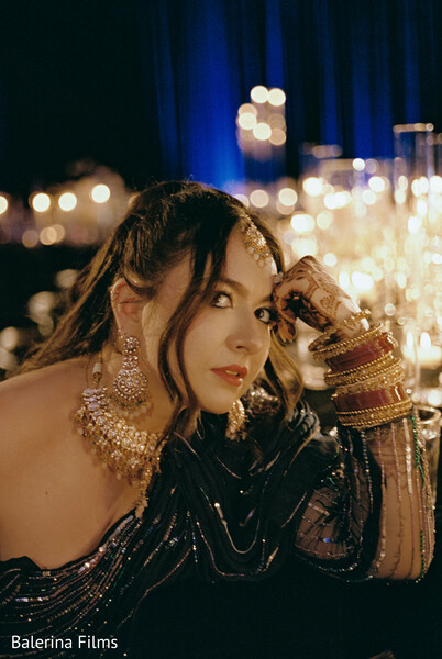 wedding guest glam,black gown style,candlelit reception,gold statement jewelry,south asian guest look,mehndi details,reception fashion,editorial wedding portrait,elegant wedding guest,moody reception lighting