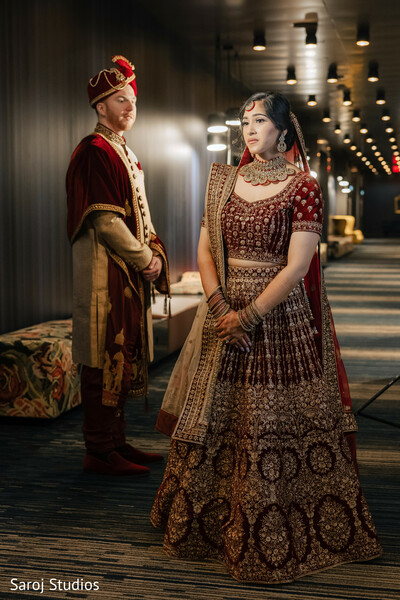 indian wedding couple,bride and groom portrait,red bridal lehenga,cream sherwani,indoor wedding photo,traditional indian attire,royal wedding look,hallway wedding portrait,luxury wedding photography,bridal jewelry details
