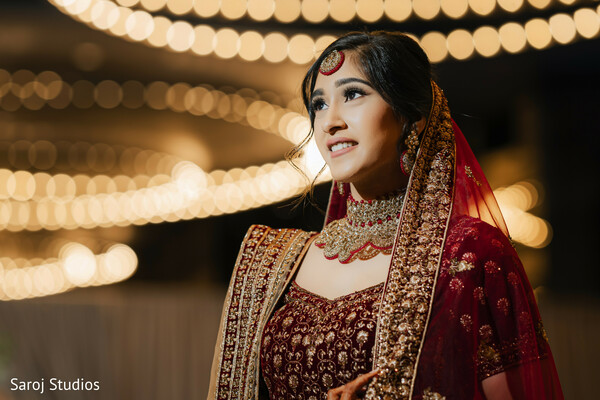 indian bridal portrait,maroon lehenga close-up,bridal dupatta shot,glowing bride,wedding lights backdrop,traditional indian jewelry,bridal makeup highlight,elegant bridal look,indian wedding photography,stunning bridal pose.