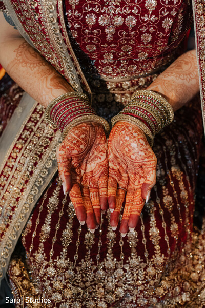bridal mehndi close-up,intricate henna designs,wedding hand jewelry,bridal bangles photo,maroon bridal lehenga detail,indian bridal traditions,henna art photography,cultural wedding shot,close-up bridal hands,traditional indian accessories.