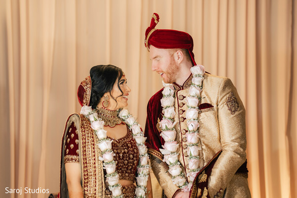 bride and groom glance,indian wedding ceremony,floral garlands couple,cream sherwani groom,red bridal lehenga,candid wedding moment,wedding love story,couple's portrait stage,sweet wedding moment,indian wedding expressions.