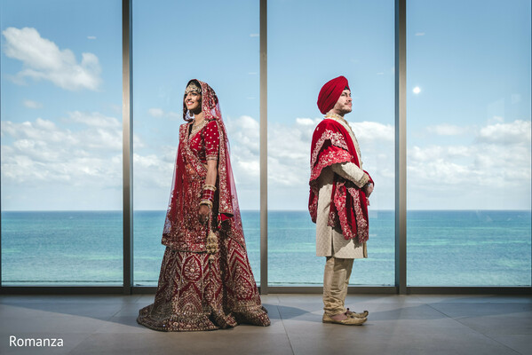 oceanfront wedding,indian couple portrait,red bridal lehenga,turban groom,destination wedding,sea view backdrop,modern wedding setting,sikh wedding attire,glass window portraits
