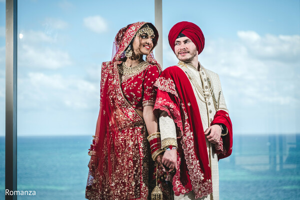 happy newlyweds,ocean backdrop,destination wedding photography,red bridal outfit,sikh groom,wedding smiles,romanza photography,glass wall,luxury wedding setting,indian wedding couple