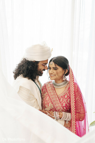 bride and groom,white drapes,pink lehenga,indian groom,romantic moment,couple portrait,bridal glow,cultural wedding,soft lighting,sweet glance