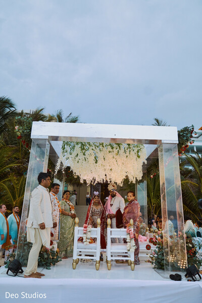 glass mandap,indian wedding ceremony,sky backdrop,modern wedding,outdoor vows,transparent decor,south asian wedding,elegant setting,spiritual moment,cultural fusion
