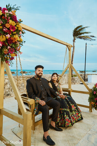 beach wedding,wooden swing,floral lehenga,seaside couple,tropical vibes,modern indian couple,outdoor photo,wedding portraits,floral decor,groom in black