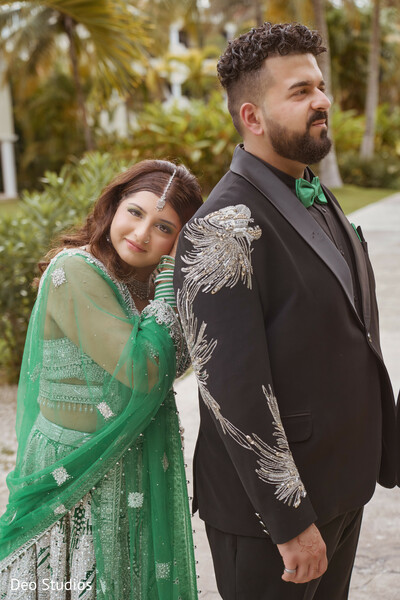 green wedding outfit,south asian couple,romantic pose,cultural fashion,modern attire,outdoor portrait,bride leaning,groom tuxedo,coordinated couple,love and support