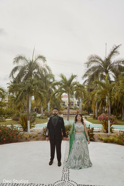 garden wedding,palm tree backdrop,green lehenga,groom suit,south asian couple,outdoor elegance,fashion-forward wedding,symmetrical shot,indian attire,modern romance