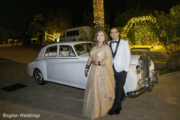 couple with vintage car,bride in gold lehenga,groom in tuxedo,wedding getaway car,luxury wedding,wedding portraits night,indian bride groom photo,glamorous wedding moment,outdoor evening wedding,wedding lights decor