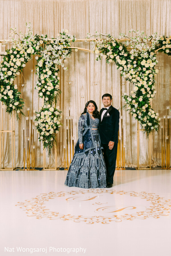 floral stage wedding photo,indian reception shoot,bride and groom formal,south asian wedding reception,luxury wedding backdrop,glamorous wedding couple,formal portrait with florals,reception photo session,elegant couple moment,floral arch wedding