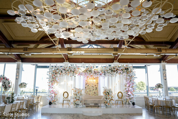 floral mandap design,wedding stage decor,luxury indoor wedding setup,modern ceiling lights,pastel floral arrangements,ceremony stage inspiration,opulent wedding design,natural light wedding photo,grand mandap setup,destination wedding decor