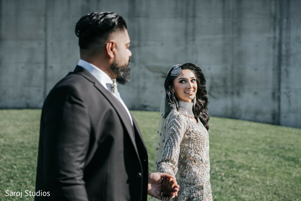 romantic wedding walk,grassy wedding venue,bride looking back pose,silver gown bride,groom in black suit,candid couple moment,outdoor wedding portrait,elegant wedding attire,joyful wedding stroll,love in motion