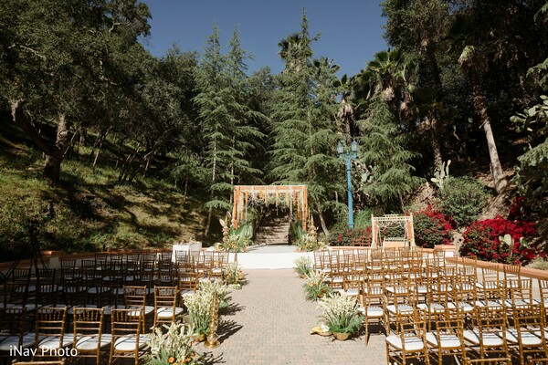 outdoor ceremony,floral mandap,forest wedding,wooden chairs,greenery wedding,scenic vows,nature ceremony setup,south asian wedding altar,romantic wedding venue,open-air ceremony