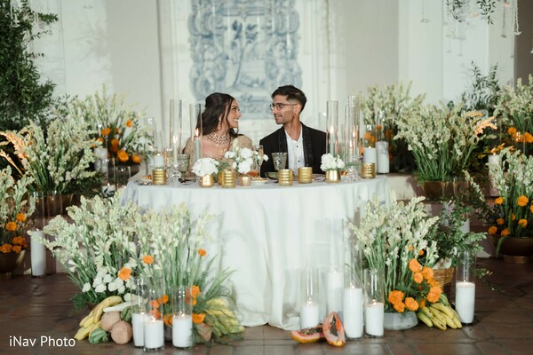 sweetheart table,bride and groom reception,floral backdrop,wedding flowers,intimate dining,newlyweds celebration,orange and white wedding theme,elegant reception decor,romantic dinner,luxury wedding details