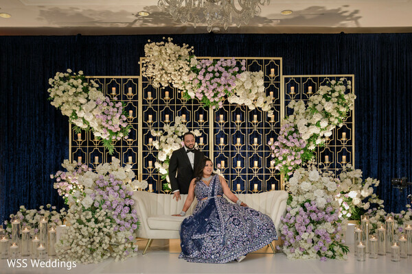 floral wedding stage,bride and groom portrait,luxury wedding decor,pastel flower arrangements,navy and gold wedding design,glamorous stage photo,south asian couple reception,romantic wedding photography,candlelit wedding setting,regal couple portrait