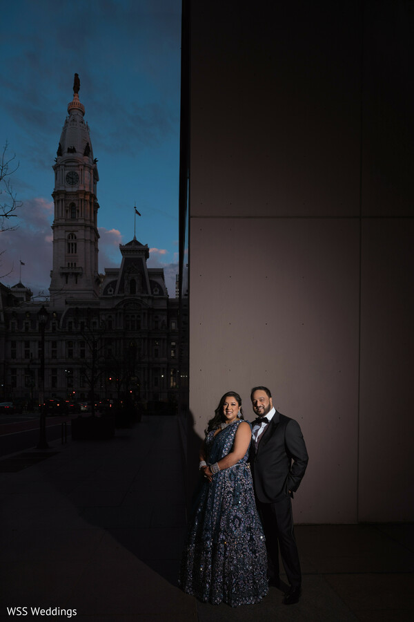 city street wedding photo,dusk wedding portrait,bride navy gown,groom tuxedo elegance,south asian couple in city,glowing city lights photo,glamorous urban portrait,romantic evening wedding,timeless couple elegance,chic city wedding style