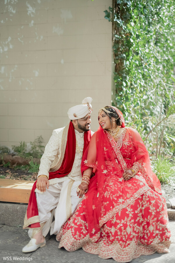 outdoor indian wedding,red bridal lehenga,ivory groom sherwani,romantic couple portrait,greenery wedding backdrop,south asian cultural attire,intimate wedding photography,natural light couple photo,elegant traditional wedding,love story moment