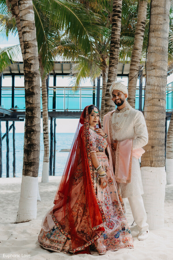 red lehenga bride,tropical wedding portrait,palm trees couple,south asian wedding attire,destination wedding,beige sherwani groom,cultural wedding shot,vibrant wedding colors,elegant bride and groom,outdoor love