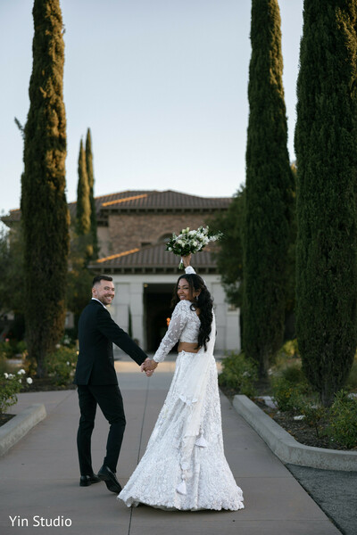 temple courtyard,indian newlyweds,coral saree bride,sherwani groom,hand in hand,cultural beauty,romantic walk,wedding portraits,elegant couple,serene moment