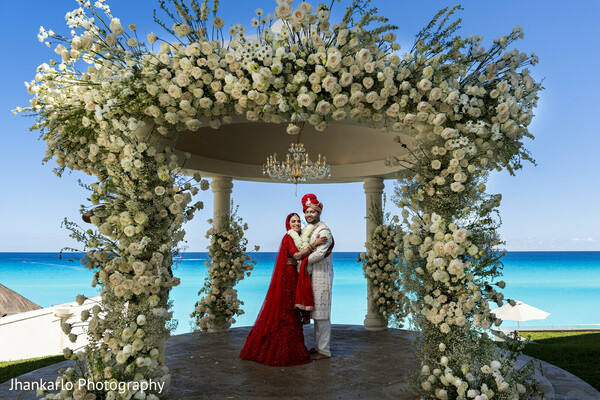 bridal portrait,red lehenga,floral arch,ocean backdrop,destination wedding,cancun bride,elegant pose,indian bride,tropical wedding,stunning setting